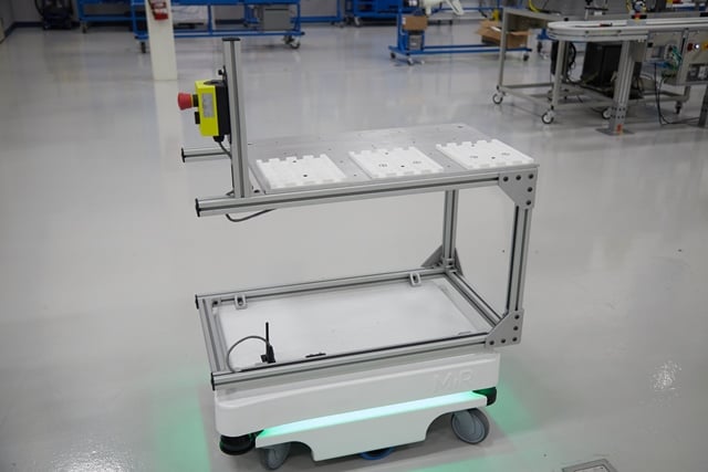 Autonomous mobile robot with a metal frame cart on a clean manufacturing floor.