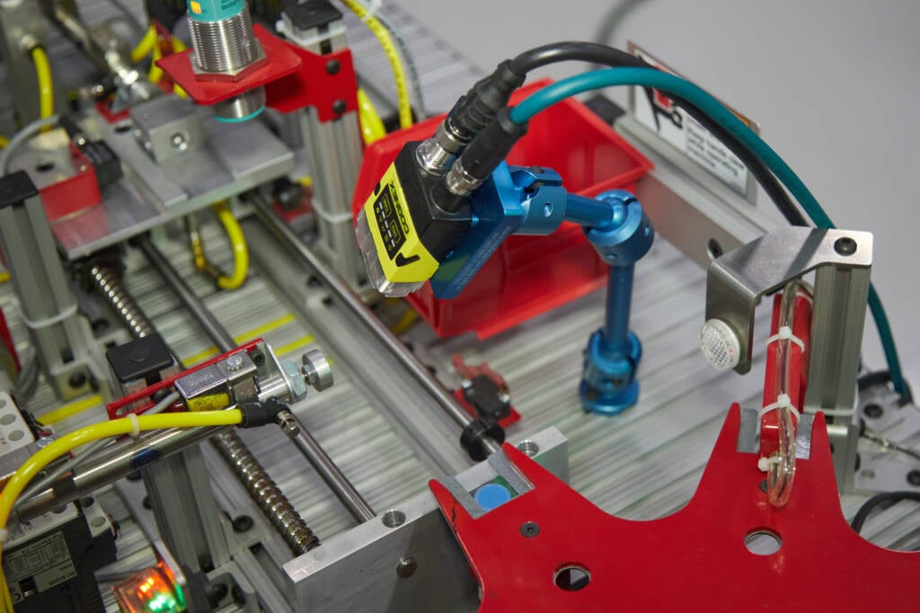 Industrial automation inside a metal frame showing red and blue robotic components and yellow cables