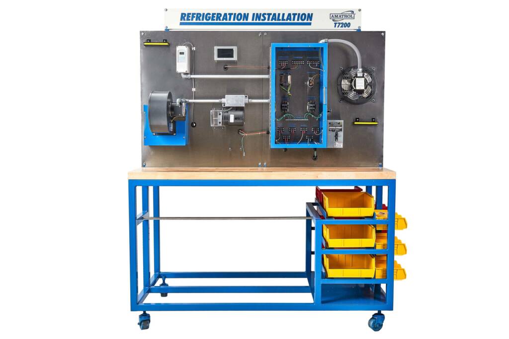 Industrial refrigeration training rig mounted on a metal board with a blue frame, showing a control panel, motor, piping, and a cooling fan on the right.