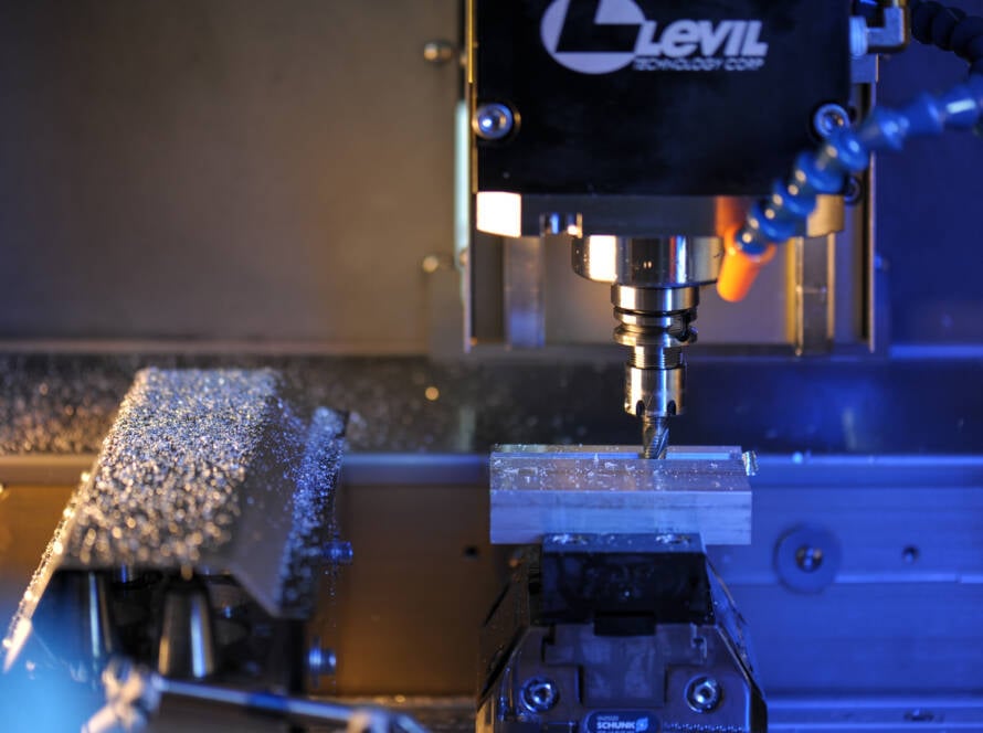Close-up of a CNC milling machine spindle cutting metal, with a blue‑tinted workspace and coolant hose on the right.