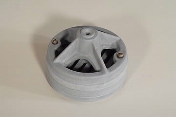 Gray circular plastic component with three radial spokes and a central hole, two screws visible on a white surface