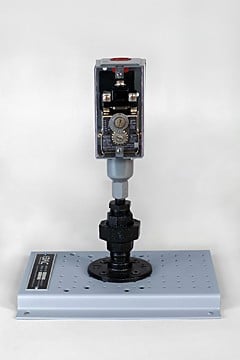 Electromechanical actuator mounted on a perforated metal base plate, with exposed gears and wiring visible in the vertical housing.