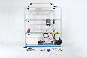 Lab-scale experimental rig on a metal frame with tubing, gauges, and a small pump; various fittings and components laid out in front for assembly or testing.
