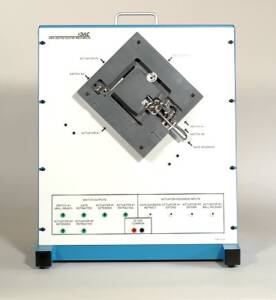 White actuation test cabinet with blue base; front panel shows a diagonal metal plate connected to actuators and solenoids for testing.