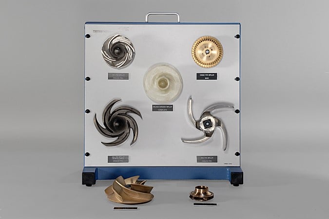 Panel-mounted assortment of turbine impellers with labels, plus two loose blades on the table.