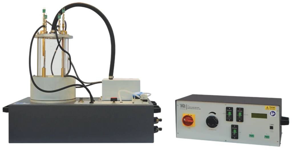 Laboratory hydraulic testing rig with a vertical piston cylinder and looping hoses connected to a separate control panel on the right.