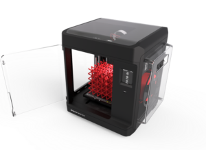 Compact black 3D printer with side door open, a red lattice object visible inside during printing.