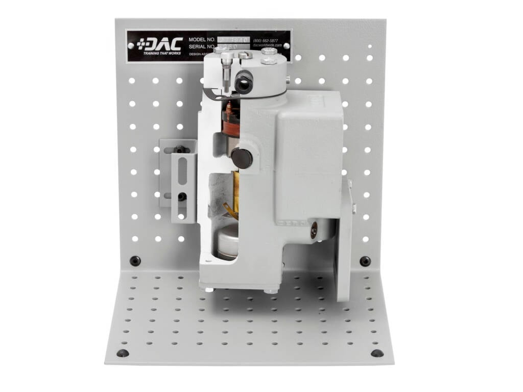 Industrial clamp/actuator mounted on a perforated metal pegboard, showing a gray mechanism and mounting hardware