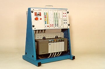 Blue industrial test equipment rack with a control panel showing colored LEDs, switches, and indicators, mounted over a beige hardware unit.
