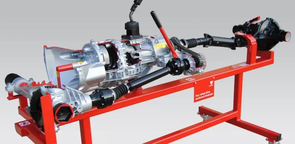 Cutaway view of a four‑wheel‑drive transmission and drive shafts mounted on a red stand, showing exposed gears and axles.