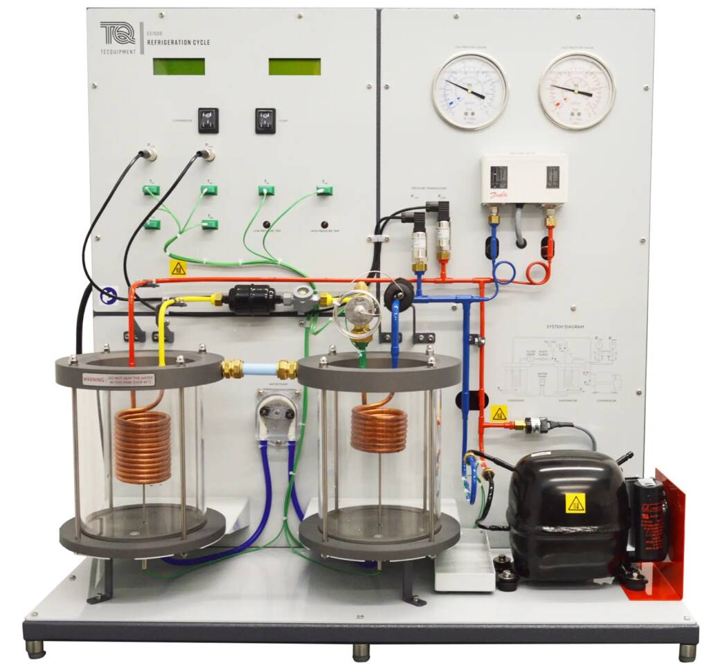 Industrial lab boiler with copper coils, glass cylinders, pipes, and a control panel with gauges on the right side