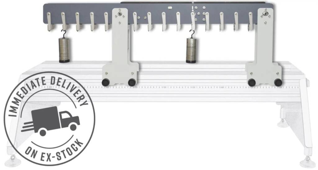Industrial fabric measuring/holding device: wide horizontal beam with multiple hooks, two hanging weights, and a long ruler scale—likely used to align or measure fabric material.